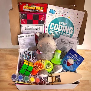 Puede incluir: Una caja de regalo llena de juguetes y actividades educativas. Incluye un juego de damas, un hipopótamo de peluche, un cubo de Rubik, un muelle, pintura y un libro de actividades de codificación STEM. También incluye un kit de volcán y nieve instantánea.