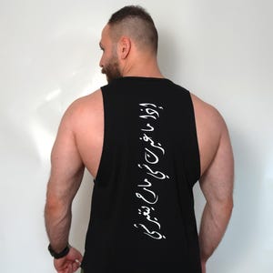 May include: Black sleeveless tank top with white Arabic script down the back. The tank top has a curved hemline and is worn with olive green shorts. The person is facing away from the camera.