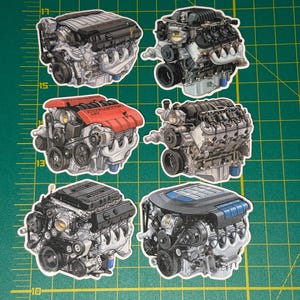 May include: Six die-cut stickers of detailed car engine illustrations. The engines are in various colors, including black, red, and blue. The stickers are arranged on a green grid background with inch measurements.