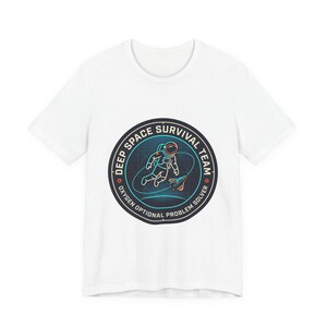 May include: White t-shirt with a circular graphic depicting an astronaut and a rocket. The graphic reads "DEEP SPACE SURVIVAL TEAM" and "OXYGEN OPTIONAL PROBLEM SOLVER". The astronaut is in a spacesuit, with a blue and orange design.
