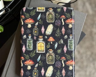 May include: A black case featuring a repeating pattern of mushrooms, crystals, and potion bottles. The case has a glossy finish and is resting on two grey books. The design includes red, white, blue, and green elements.