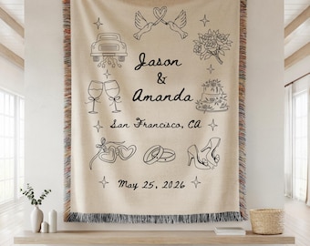 May include: A beige woven throw blanket with black line art illustrations of wedding-related symbols. The blanket features the names "Jason & Amanda", the location "San Francisco, CA", and the date "May 25, 2026". The blanket has a fringed edge.
