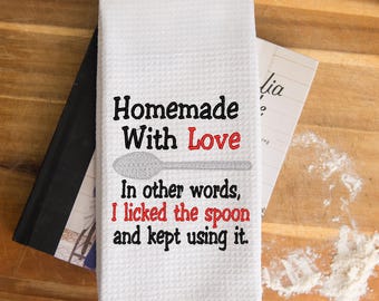 May include: A white waffle-weave kitchen towel featuring black and red embroidered text that reads: Homemade With Love, In other words, I licked the spoon and kept using it, accompanied by a grey embroidered spoon graphic centered on the fabric.