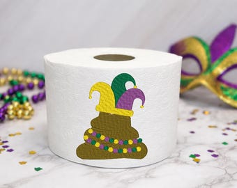 May include: A white toilet paper roll featuring an embroidered design of a brown poop emoji wearing a yellow, green, and purple jester hat. The embroidered poop emoji is also decorated with a string of yellow, green, and purple Mardi Gras beads.