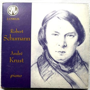 Può includere: Una copertina di un album vintage con un ritratto di Robert Schumann e il nome di André Krust. La copertina ha uno sfondo viola con scritte dorate. L'album è etichettato "piano" e ha il logo B&W.