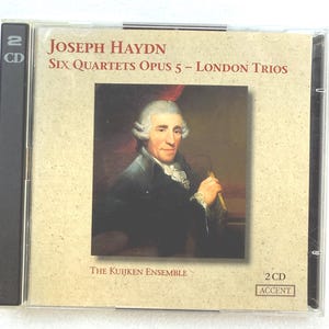 May include: A CD case featuring the album "Joseph Haydn: Six Quartets Opus 5 - London Trios" by The Kuijken Ensemble. The cover art includes a portrait of a man in a white wig. The case indicates it contains 2 CDs.