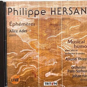May include: A CD case featuring the title "Philippe HERSANT" in large, bold letters. The cover includes the text "Éphémères" and "Musical humors", along with the names of performers and the orchestra. The background has a textured, wood-like appearance.