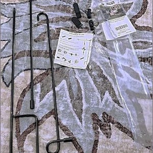 May include: A collection of black metal garden flag poles and accessories, including hooks, connectors, and a set of instructions. The items are arranged on a patterned surface, with some components still in packaging.