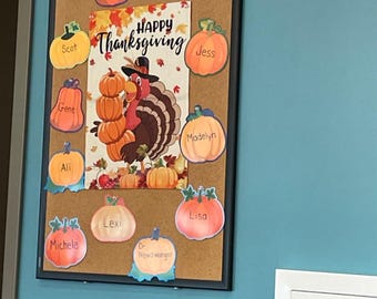 May include: A corkboard with a black frame, decorated for Thanksgiving. It features pumpkin cutouts with names, a turkey graphic, and the words "Happy Thanksgiving."
