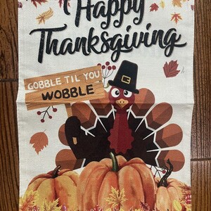 Könnte beinhalten: Dekoratives Banner zum Thema Thanksgiving mit dem Schriftzug "Happy Thanksgiving" in schwarzer Schrift. Ein Cartoon-Truthahn mit einem Pilgerhut hält ein Schild mit der Aufschrift "Gobble Til You Wobble". Kürbisse und Herbstblätter ergänzen das Design.