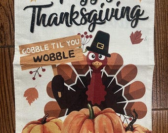 May include: Thanksgiving-themed decorative banner with the words "Happy Thanksgiving" in black script. A cartoon turkey wearing a pilgrim hat holds a sign that says "Gobble Til You Wobble". Pumpkins and autumn leaves complete the design.