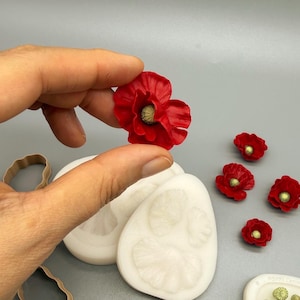 Puede incluir: Un juego de moldes de silicona blanca para manualidades de amapolas, que incluye cuatro cortadores de metal color cobre, cuatro pequeños adornos de amapola roja con centros verdes y un molde blanco pequeño con cinco formas de cápsulas de amapola.