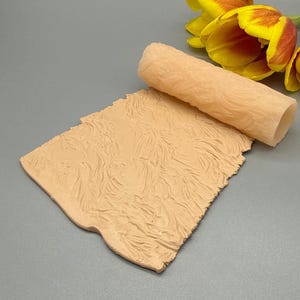 Peut inclure: Une feuille de silicone texturée de couleur beige et un tube roulé. La feuille et le tube présentent un motif ondulé. Des tulipes jaunes et rouges sont en arrière-plan. Il s'agit de fournitures artisanales.