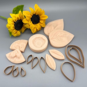 May include: A collection of light peach-colored silicone molds and brown plastic petal cutters for crafting floral shapes, accompanied by two bright yellow sunflowers with dark brown centers positioned at the top left of the arrangement.