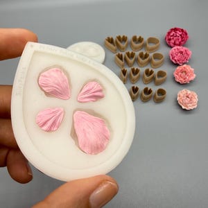 May include: A white silicone mold for peony petals with the text Silky Petals Peony Petals Mini & Midi, featuring four pink petal impressions. Beside it are several brown petal cutters and four finished pink peony flower decorations.