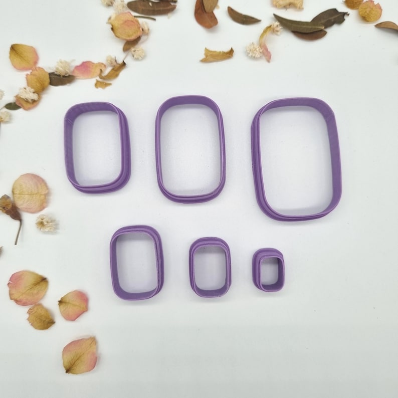 May include: A set of six purple rectangular cookie cutters with rounded corners, arranged in a descending size order. The cutters feature a simple, open-frame design with a consistent thickness, providing a clear view of the hollow center.