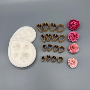 May include: A white silicone mold with petal impressions, sixteen brown plastic petal cutters arranged in four rows of four, and four finished artificial flowers in shades of pink, ranging from deep magenta to a light, pale blush color.