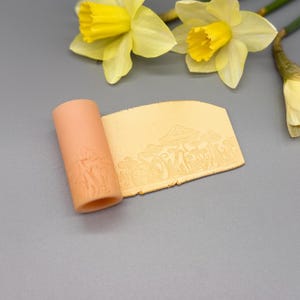 May include: A peach-colored cylindrical clay roller featuring an embossed mushroom forest pattern, accompanied by a flat, rectangular piece of light yellow clay that displays the same detailed mushroom design pressed into its surface.