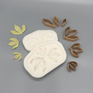 May include: Two white rectangular silicone molds with leaf impressions, accompanied by several brown plastic leaf-shaped cutters and three small, light green, textured leaf-shaped cutouts arranged on the left side of the composition.