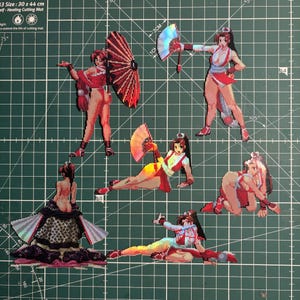 May include: A selection of pixel art stickers depicting female characters in dynamic poses. The stickers feature characters in red and white attire, some with fans or parasols. The art style is reminiscent of classic video games.