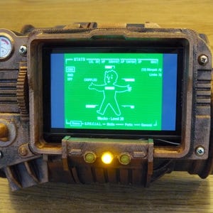 Op de afbeelding: Een bruin en bronzen rekwisiet met een groen scherm met een omtrek van een personage. Het apparaat heeft een meter, knoppen en een scherm met spelstatistieken. Het scherm toont de tekst "Wacks - Level 20".