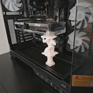 May include: A white 3D-printed statue of a figure holding up a platform, placed inside a black computer case. The case has multiple fans and a graphics card with the "MSI" logo. The overall theme is technology and decor.