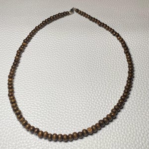 May include: A brown wooden bead necklace. The necklace is composed of small, round, dark brown beads strung together. The necklace is displayed on a white surface.