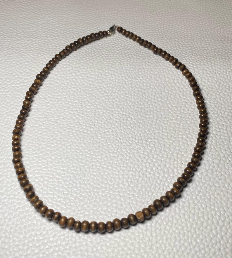 May include: A brown wooden bead necklace. The necklace is composed of small, round, dark brown beads strung together. The necklace is displayed on a white surface.