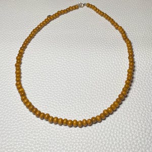 May include: A necklace featuring small, round, golden-brown beads. The beads are strung together, forming a complete circle. The necklace has a silver clasp. The jewelry is displayed on a white surface.