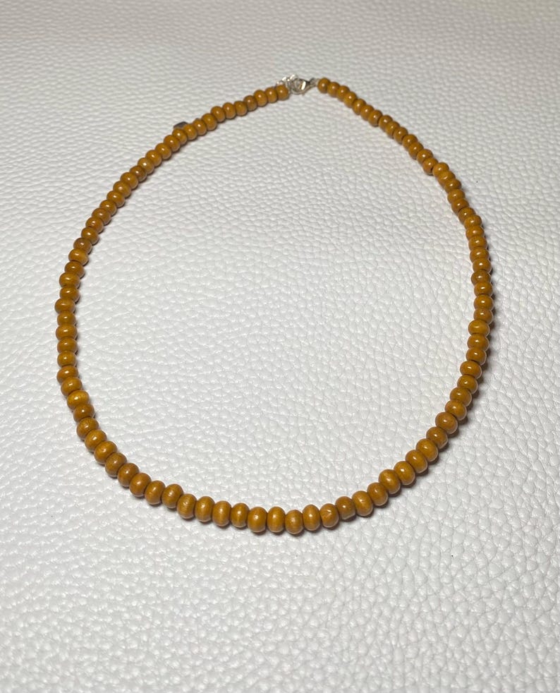 May include: A necklace featuring small, round, golden-brown beads. The beads are strung together, forming a complete circle. The necklace has a silver clasp. The jewelry is displayed on a white surface.