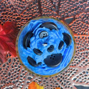 Top view of Coraline-inspired Halloween candle with button portal design, blue whipped cream topping, and creepy cute spooky season decor vibes.