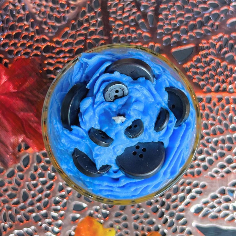 Top view of Coraline-inspired Halloween candle with button portal design, blue whipped cream topping, and creepy cute spooky season decor vibes.