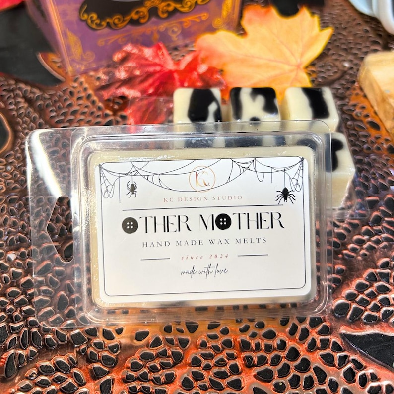 Other Mother wax melt with black syrup swirl and black buttons, square soy wax melt on autumn leaves background, Coraline inspired spooky Halloween home fragrance