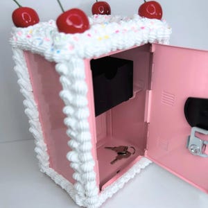Open pink cake vault mini locker showing basket for coins and spacious bottom compartment for cash or jewelry.