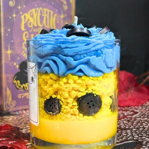 Side view of Coraline candle showing yellow layers for raincoat, black button ring detail, and hand-poured soy wax in Halloween limited edition jar.