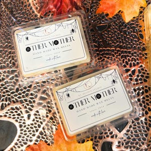 Two Other Mother wax melts with black syrup swirls and black button accents, square soy wax melts on wooden surface, Coraline inspired spooky Halloween home fragrance.