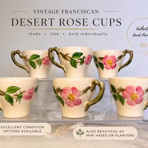 May include: Vintage Franciscan Desert Rose cups. These hand-painted cups from the 1940s feature a cream-colored base with pink rose and green leaf designs. The handles have a gold-colored finish. Sold individually, these cups are also beautiful as mini vases or planters.