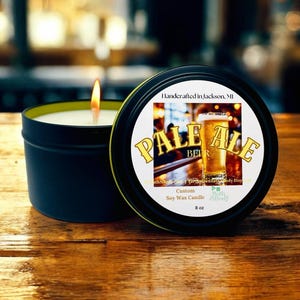 May include: A black candle tin with a lit wick, next to its lid. The lid features a label with "PALE ALE BEER" text and a beer glass image. The candle is labeled "Custom Soy Wax Candle" and is 8 oz.