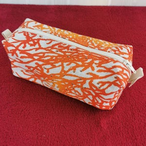 Puede incluir: Bolsa rectangular con cremallera con un diseño de arrecife de coral en naranja y blanco. La bolsa tiene una cremallera blanca y un pequeño lazo de tela. El fondo es rojo liso.