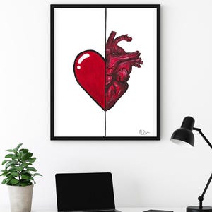 May include: Framed art print showing a split heart design. One half is a stylized red heart, the other a detailed anatomical heart. The artwork is in a black frame, displayed on a white wall.