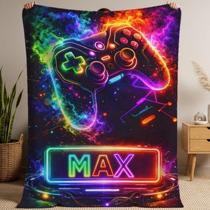 May include: A rectangular fleece blanket featuring a vibrant, neon-colored gaming controller graphic surrounded by swirling clouds of smoke and light. Below the controller, a glowing rectangular frame contains the name MAX in bold, bright letters.