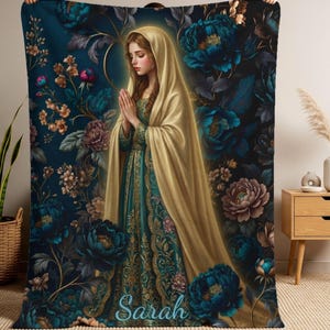 May include: A plush blanket featuring a detailed illustration of a woman in a gold head covering and teal dress, with hands clasped in prayer. The background is a dark teal with floral accents, and the name "Sarah" is written in script.
