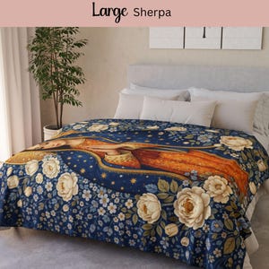 May include: A large Sherpa blanket with a floral design featuring a central figure in orange and gold, surrounded by white roses and blue flowers on a navy blue background. The blanket is draped over a bed with white pillows.