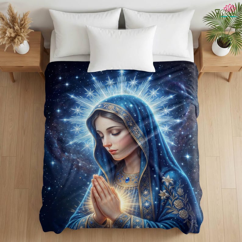 May include: A blue and gold blanket featuring an illustration of a woman with a blue veil, hands clasped in prayer. The background is a starry night sky with a bright halo around the woman's head. The blanket is on a bed with white pillows.