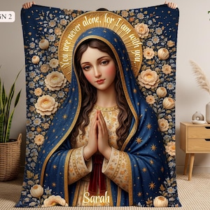 May include: A blue blanket featuring a religious illustration of a woman with a halo, hands clasped in prayer. The design includes floral patterns and the text "You are never alone, for I am with you." The name "Sarah" is also visible.