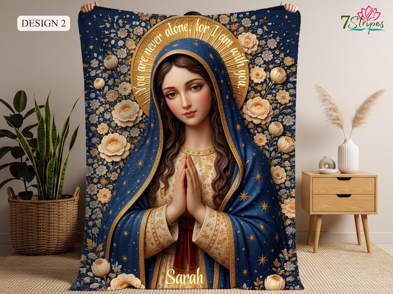 May include: A blue blanket featuring a religious illustration of a woman with a halo, hands clasped in prayer. The design includes floral patterns and the text "You are never alone, for I am with you." The name "Sarah" is also visible.