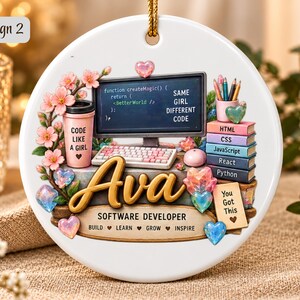 Może przedstawiać: Okrągła biała ceramiczna ozdoba z monitorem komputerowym wyświetlającym kod, klawiaturą, r&oacute;żowym kubkiem z napisem 'CODE LIKE A GIRL' oraz stosem książek 'HTML', 'CSS', 'JavaScript', 'React', 'Python'. Imię 'Ava' jest wyśrodkowane, poniżej 'SOFTWARE DEVELOPER' i 'BUILD LEARN GROW INSPIRE', otoczone r&oacute;żowymi kwiatami i sercami.