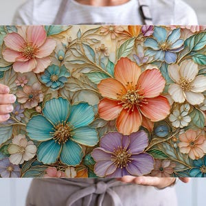 Puede incluir: Una obra de arte floral rectangular con una variedad de flores coloridas en tonos de rosa, naranja, azul y morado. Las flores tienen contornos dorados y están sobre un fondo crema. La obra de arte es sostenida por una persona.