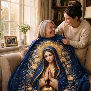 May include: A blue blanket featuring an image of the Virgin Mary with a gold halo and floral accents. The blanket is draped over two people on a sofa. The blanket has the text "Never Alone, I am with you".
