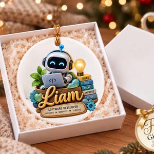 Może przedstawiać: Okrągła biała ceramiczna ozdoba przedstawiająca robota w słuchawkach, piszącego na laptopie z symbolem kodu. Imię Liam jest napisane złotą czcionką nad tekstem Software Developer, Automate, Innovate, Elevate.